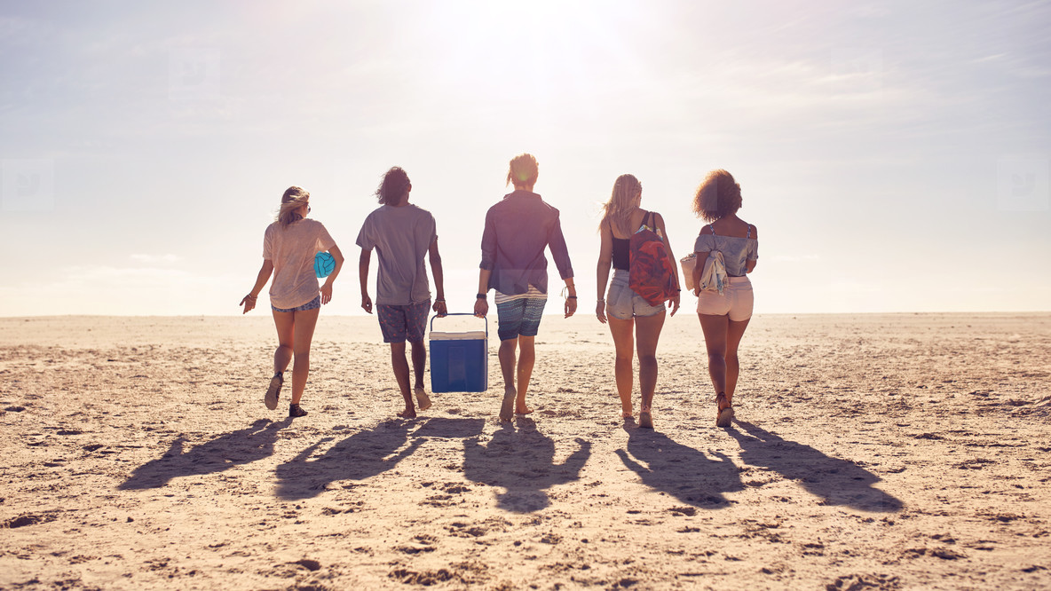 Friends walking on the beach carrying a cooler box