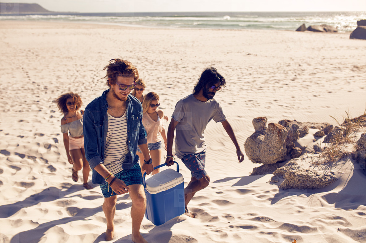 Group of friends carrying cooler to party on beach