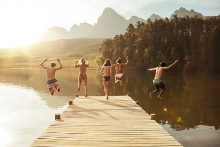 Group of young people jumping into the water from a jetty