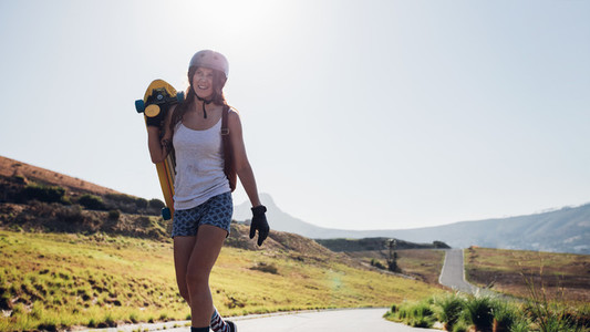 Woman walking with a longboard on countryside road