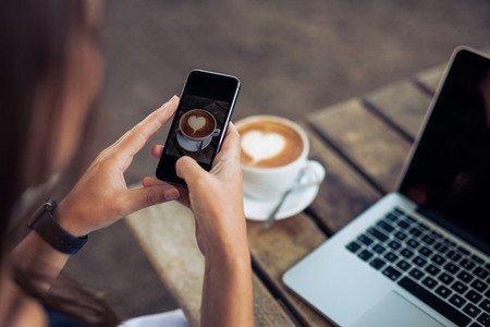 Woman photographing a coffee of cup with smart phone
