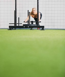 Fit young female using prowler exercise equipment at gym