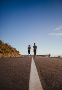 Two young people jogging on country road
