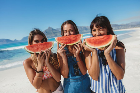 Young women having fun on the beach and eating watermelon