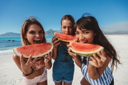 Three young women enjoy fresh watermelon on beach