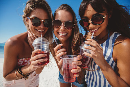 Beautiful young women drinking cold beverage on the beach