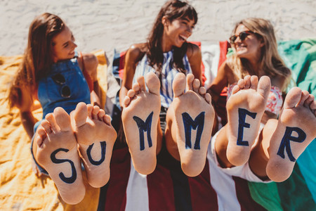 Bare feet of female friends with word summer
