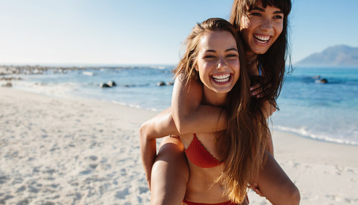 Beach vacation young woman carrying her friend on back