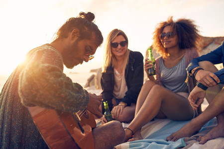 Hipster playing guitar for friends at the beach