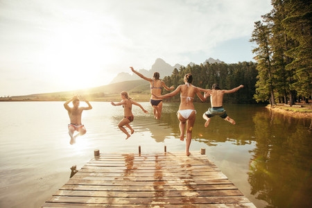 Friends jumping into the water from a jetty