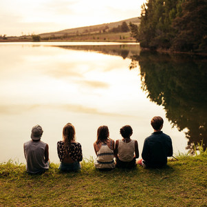 Group of young friends sitting in a row by a lake