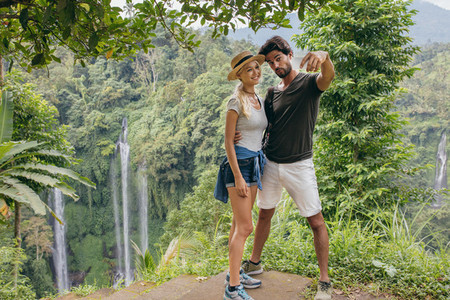 Beautiful couple together on cliff taking selfie with waterfall
