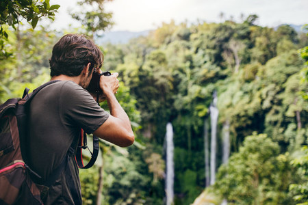Male hiker photographing a waterfall in forest