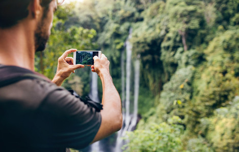 Man taking photos of waterfall with his cellphone