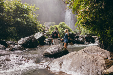 Young couple crossing stream in forest