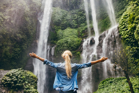 Woman standing by waterfall with her hands raised