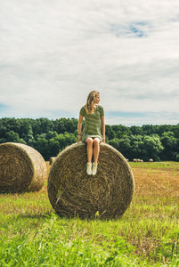 Young blond lady sitting on haystack and looking away Hungary