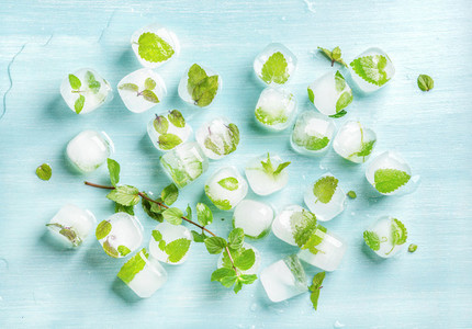 Ice cubes with frozen mint leaves inside on blue Turquoise background  top view