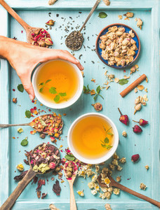 Two cups of healthy herbal tea with mint  cinnamon  dried rose  camomile flowers in spoons and man039 s hand holding spoon