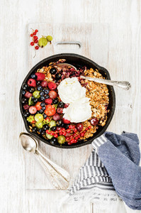 Oat granola crumble with berries and ice cream over white backdrop
