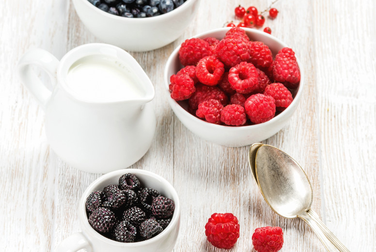 Fresh berries and milk in pitcher on white wooden background