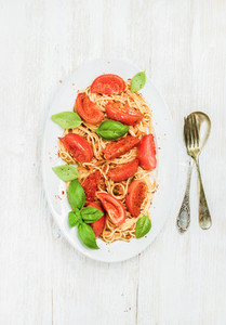 Pasta with roasted tomatoes and basil over white wooden background