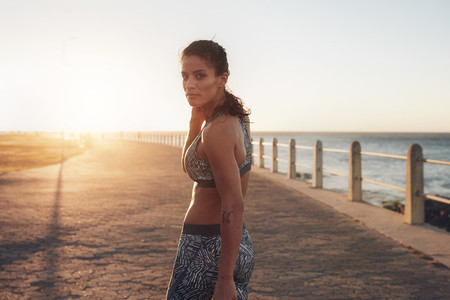 Muscular young woman in sportswear walking by the sea