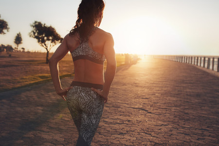 Sportswoman walking on a seaside promenade at sunset