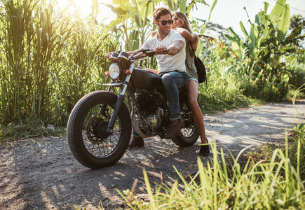 Young couple straddling motorbike on rural road