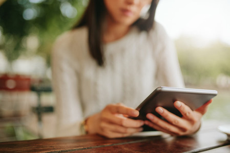 Young female sitting at cafe table with digital tablet