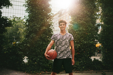 Young man holding a basketball on outdoor court