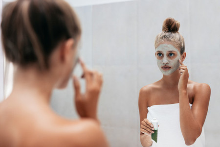 Young woman applying facial mask
