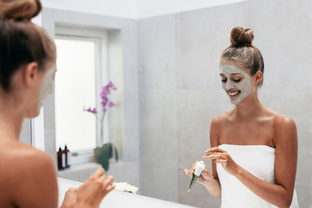 Young woman applying face mask in bathroom