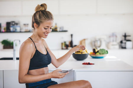 Smiling woman in kitchen using mobile phone