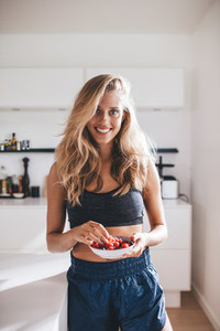 Beautiful young woman in kitchen with a bowl of fresh berries