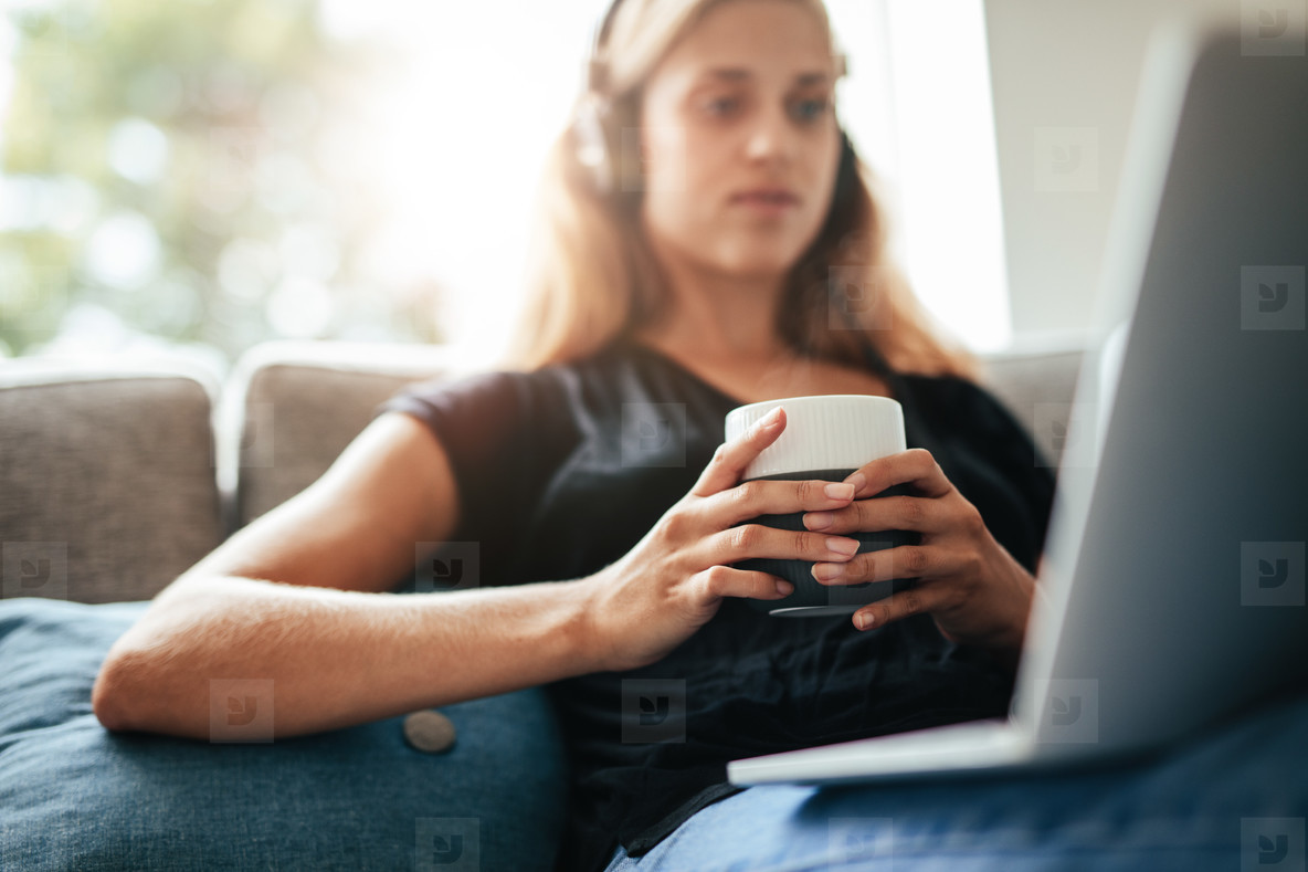 Cup of coffee in hands of a woman relaxing on sofa