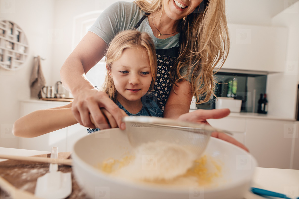 Little girl learning to make batter from her mother