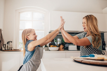 Little girl and her mother in kitchen giving high five