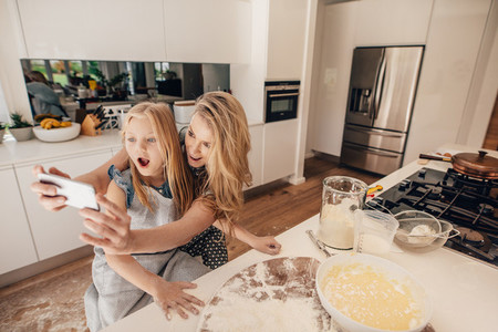 Mother taking selfie with her daughter in kitchen