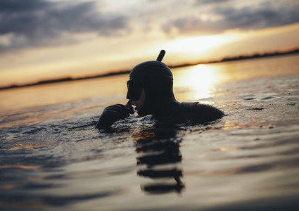 Young adult snorkeling in sea during sunset