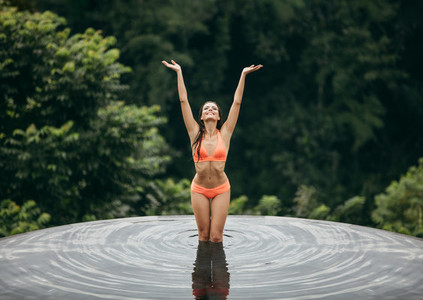 Bikini woman standing in pool with hands raised