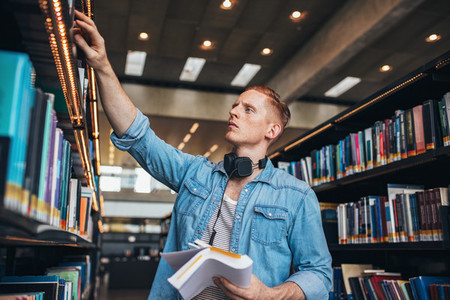 Male student selecting book from library shelf