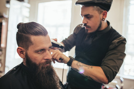 Young bearded man getting haircut in salon
