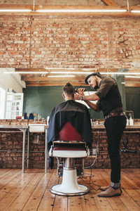 Male hairdresser trimming hair of customer