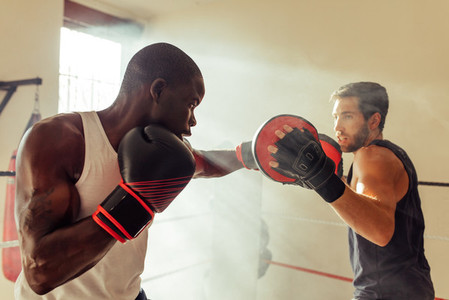 Man hitting focus mitts of boxing trainer