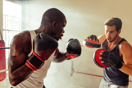 Boxing trainer with athlete practicing in gym