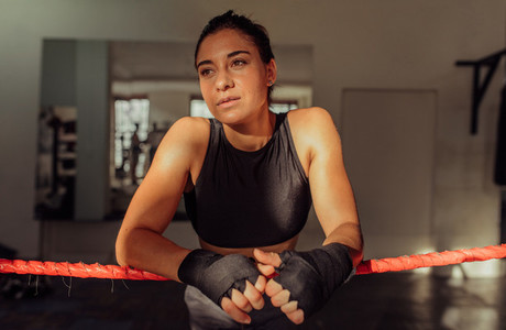 Thoughtful female boxer leaning on ropes
