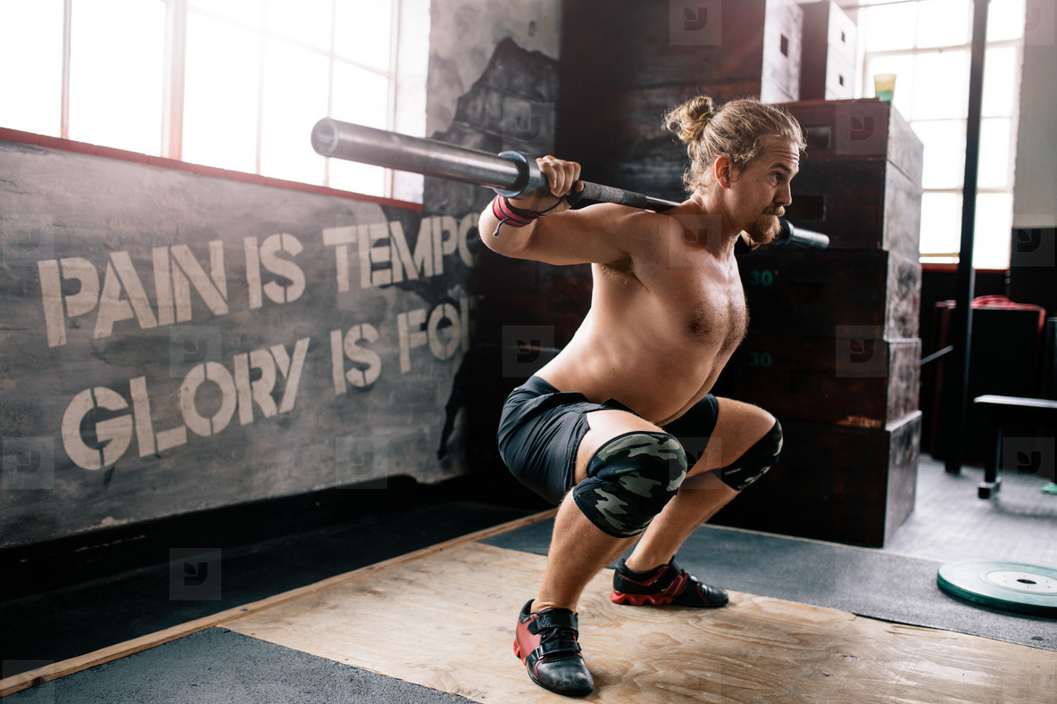 Muscular man doing squats with barbell in gym