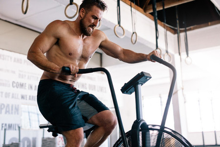 Strong man riding on exercise bike in gym