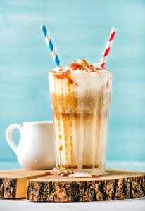 Latte macchiato with whipped cream and caramel sauce in tall glass on wooden board over blue painted wall background